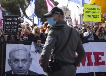 A file photo of a police officer standing guard in front of protesters as Prime Minister Benjamin Netanyahu's motorcade arrives at the District Court in Jerusalem for a hearing in his corruption trial.