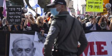 A file photo of a police officer standing guard in front of protesters as Prime Minister Benjamin Netanyahu's motorcade arrives at the District Court in Jerusalem for a hearing in his corruption trial.