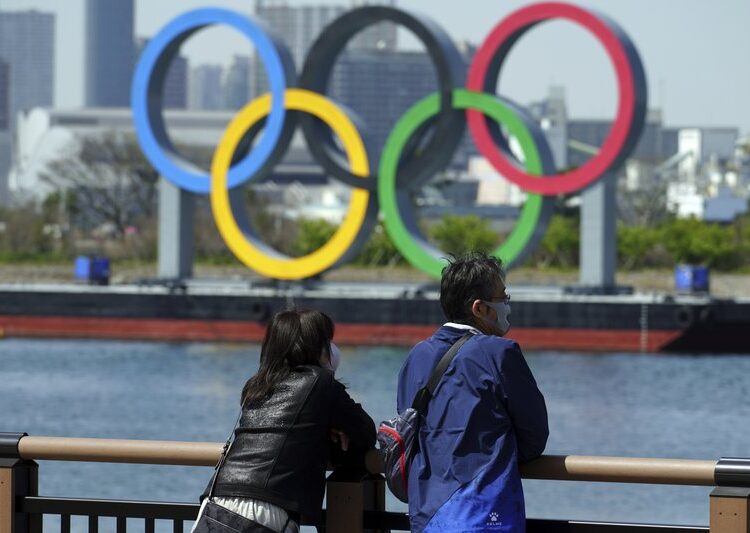 A file photo showing a man and a woman stand with a backdrop of the Olympic rings floating in the water in the Odaiba section on March 18, 2021, in Tokyo.