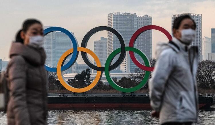 People wearing face masks walk past the Olympic Rings on January 22, 2021 in Tokyo, Japan.