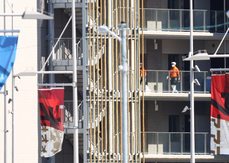 Cleaners wearing protective face masks are seen at the Athletes Village, where two athletes have tested positive for Covid-19.