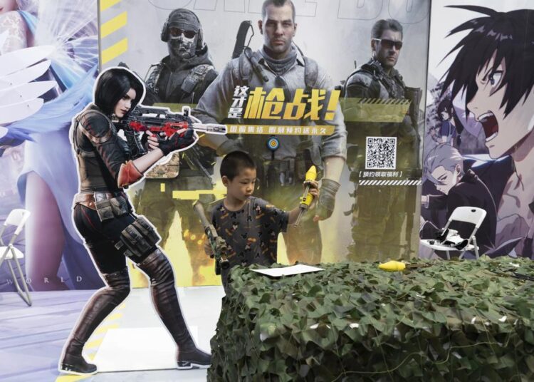 A child plays with a toy gun during a promotion for online games in Beijing on Saturday, Aug. 29, 2020. China is banning children from playing online games for more than three hours a week, the harshest restriction so far on the game industry as Chinese regulators continue cracking down on the technology sector.