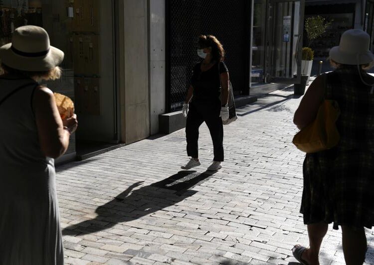 A woman wearing a face mask and gloves walks on Ermou Street, Athens' main shopping, Tuesday, Aug. 24, 2021. Greece's health minister is announcing new measures for the non-vaccinated, as the number of Covid-19 cases and hospitalizations continue to rise.