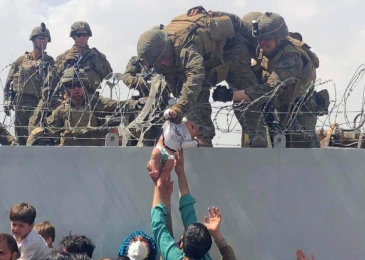 Gunfire at Kabul airport kills 1 amid chaotic evacuations 1 - Egyptian Gazette Photo shows a baby being lifted across a wall at Kabul Airport in Afghanistan by US soldiers on Thursday, Aug. 19, 2021.