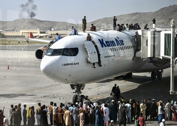 Afghan people climb atop a plane as they wait at the Kabul airport in Kabul on August 16, 2021, after a stunningly swift end to Afghanistan's 20-year war, as thousands of people mobbed the city's airport trying to flee the group's feared hardline brand of Islamist rule. (Photo by Wakil Kohsar / AFP)