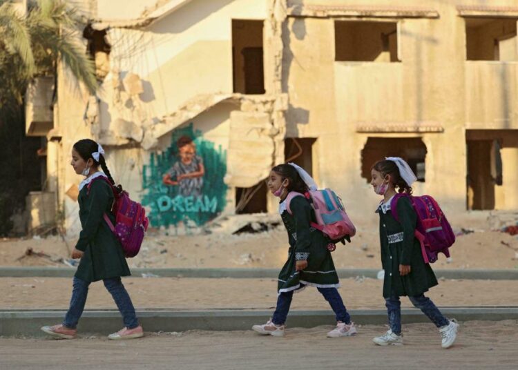 Palestinian children walk past a destroyed building on their way to school for the first day of the new scholastic year in Gaza City on August 16, 2021.