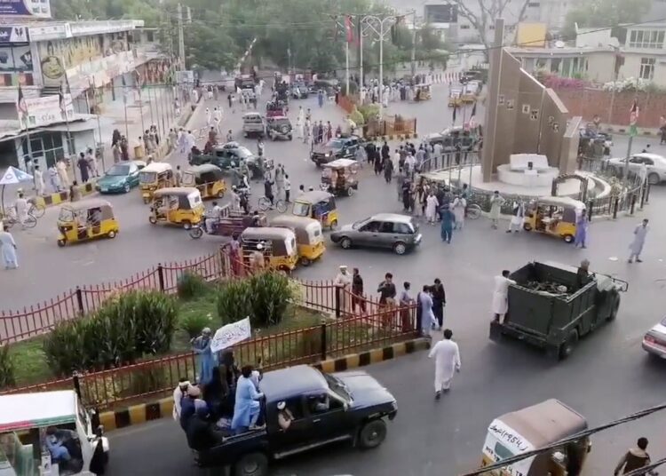 Taliban militants waving a Taliban flag on the back of a pickup truck drive past a crowded street at Pashtunistan Square area in Jalalabad, Afghanistan