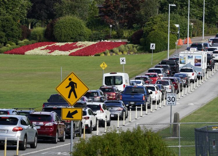 Canada reopens its border for vaccinated US visitors 1 - Egyptian Gazette A line of vehicles wait to enter Canada at the Peace Arch border crossing in view of a Canadian flag made of flowers on Aug. 9, 2021, in Blaine, Wash.