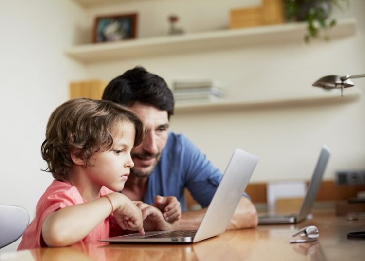 Mid adult man assisting son in using laptop at table. It is very important to make children aware of the dangers of the internet from an early age.