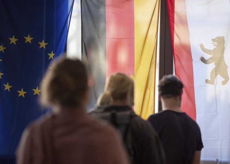 Voters stand in front of a European, German and Berlin flag at a polling station to cast their votes in Berlin, Germany, Sunday, Sept. 26, 2021. German elect a new national parliament.