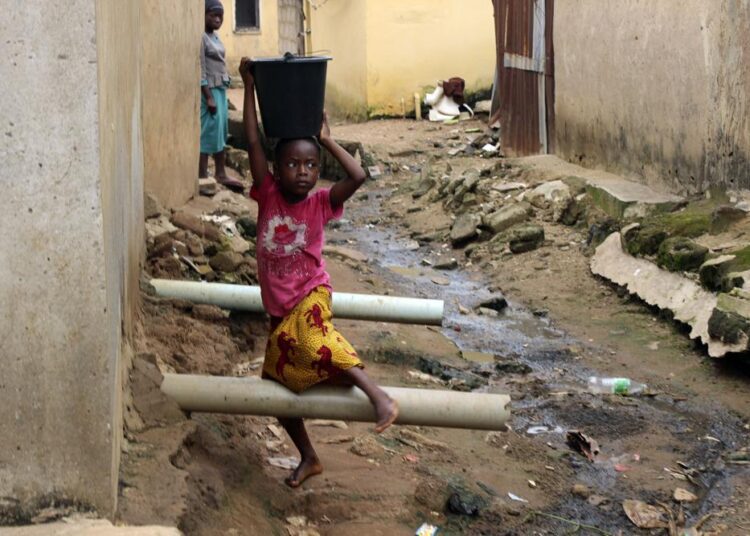A girl carrying water on her head walking past sewage around houses in Abuja, Nigeria.