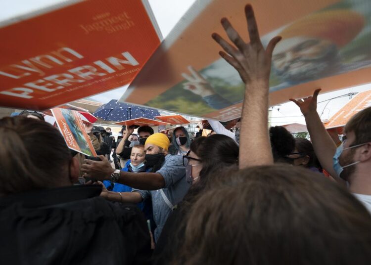 New Democratic Party supporters use signs as rain shields as NDP Leader Jagmeet Singh greets people during a campaign stop in Pitt Meadows, British Columbia, Sunday, September 19, 2021.