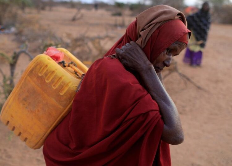 A file photo of an internally displaced woman from drought hit area carrying a jerrycan of water as she walks towards her shelter at a makeshift settlement area in Dollow, Somalia.