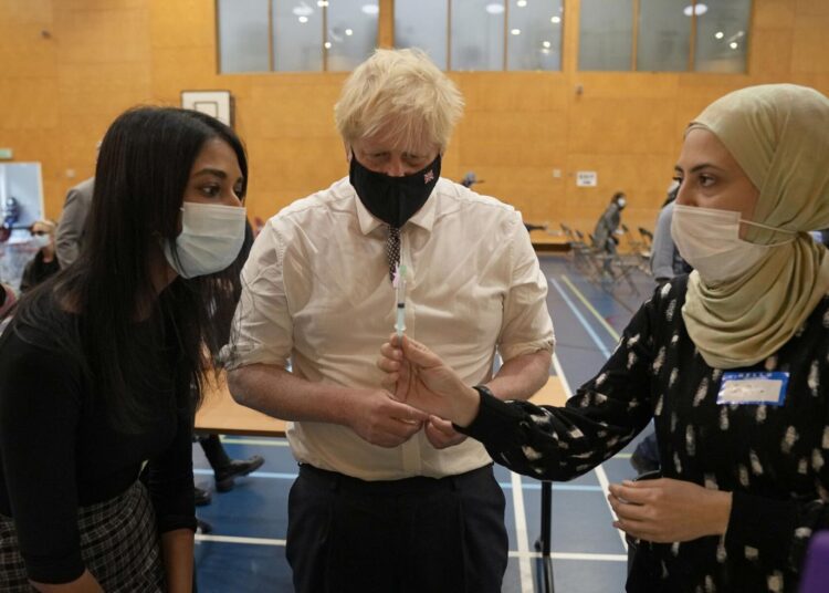 British Prime Minister Boris Johnson watches as staff dilute a dose of the Pfizer vaccine before administering it as he visits a COVID-19 vaccination centre at Little Venice Sports Centre, in London, Friday, Oct. 22, 2021.