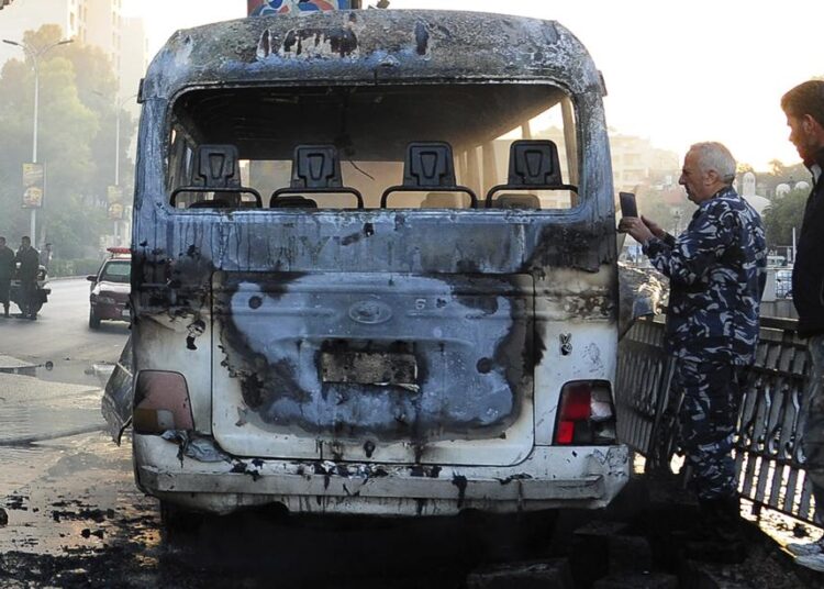 In this photo released by the Syrian official news agency SANA, Syrian security officers gather around a burned bus at the site of a deadly explosion, in Damascus, Syria, Wednesday, Oct. 20, 2021. Two roadside bombs exploded near a bus carrying troops during the morning rush hour in the Syrian capital early Wednesday, killing and wounding several people, state TV reported.
