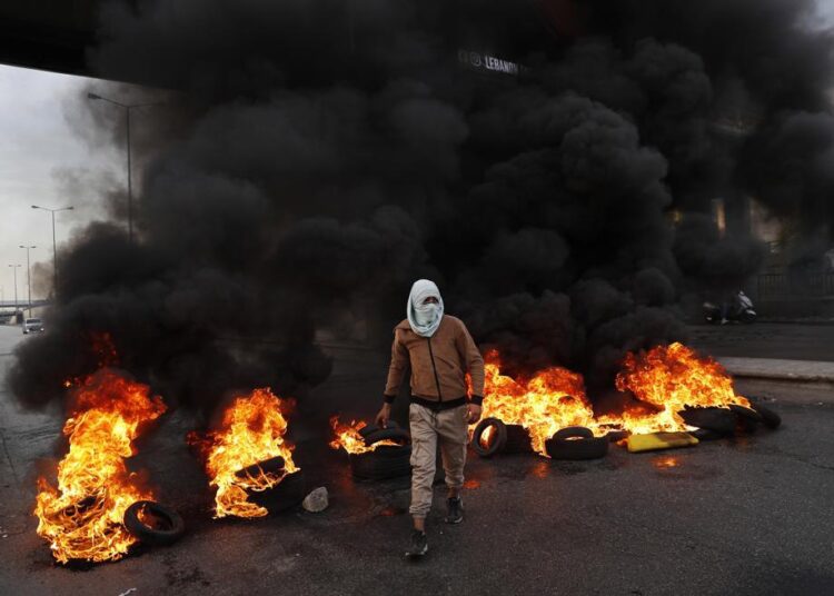 A protester passes burning tires along a main highway that leads to Beirut's international airport during a protest against the increasing prices of consumer goods and the crash of the local currency in Beirut, Lebanon, Monday, Nov. 29, 2021.