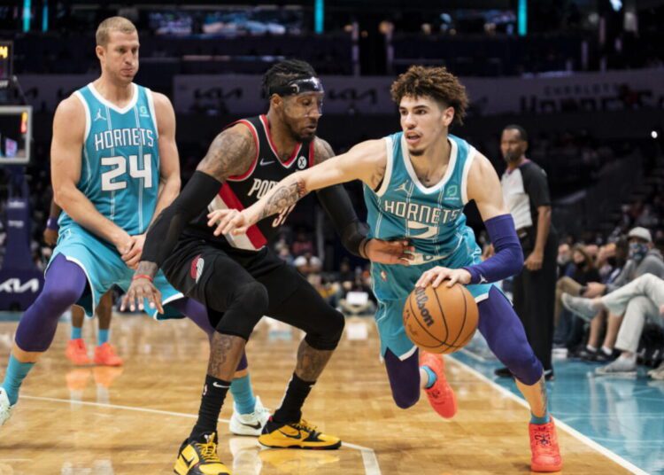 Charlotte Hornets LaMelo Ball (R) drives around Portland Trail Blazers Robert Covington (C) during the first-half of an NBA game, in Charlotte.