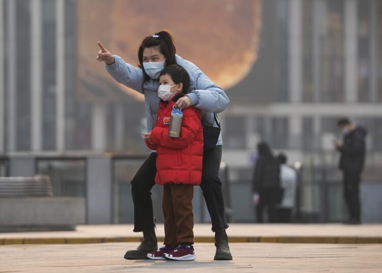 A woman and a child, both wearing face masks to protect from COVID-19 look at a commercial office building in Beijing, Sunday, Nov. 28, 2021.