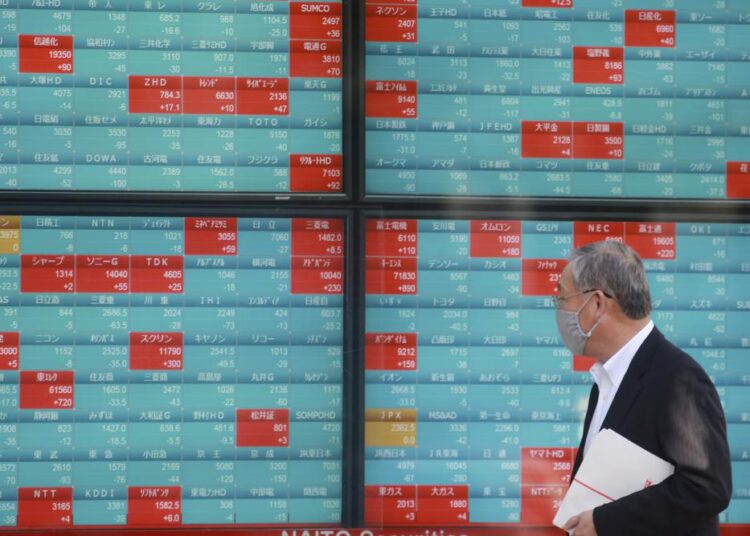 A man walks past an electronic stock board of a securities firm in Tokyo, Monday, Nov. 29, 2021. Asian stock markets fell further Monday after the omicron variant of the coronavirus was found in more countries and governments imposed travel controls.