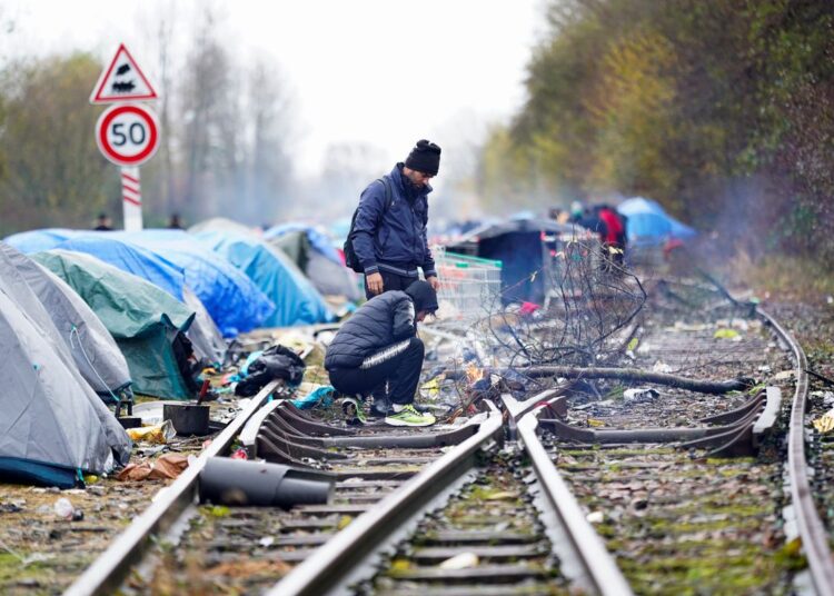 French police evict migrants from camp on Channel coast 1 - Egyptian Gazette Migrants standing near a fire on abandoned train tracks at a makeshift migrant camp at Loon Beach in Dunkirk, France.