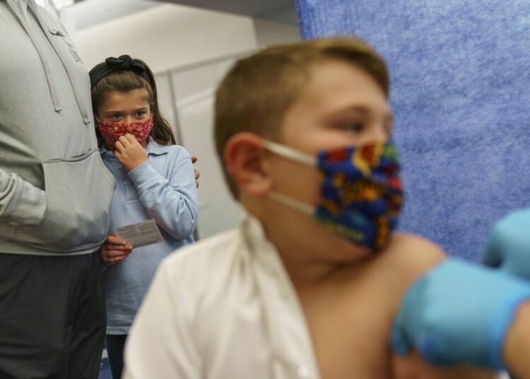 Michael Farias (L) holds his daughter, McKenzie, 8, as she watches her brother, Mikey, 10, receive the Pfizer COVID-19 vaccine for children ages 5 to 11 at a state-run site in Cranston, Rhode Island, Nov. 4, 2021.