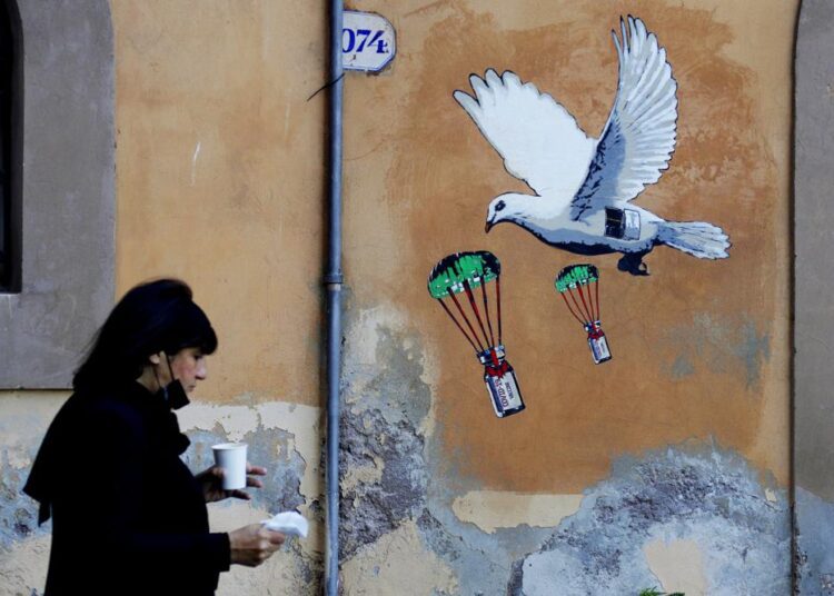 A file photo of a woman walking past a mural depicting a white dove parachuting Covid-19 vaccine vials, posted near the Italian Health Ministry Headquarters in Rome.