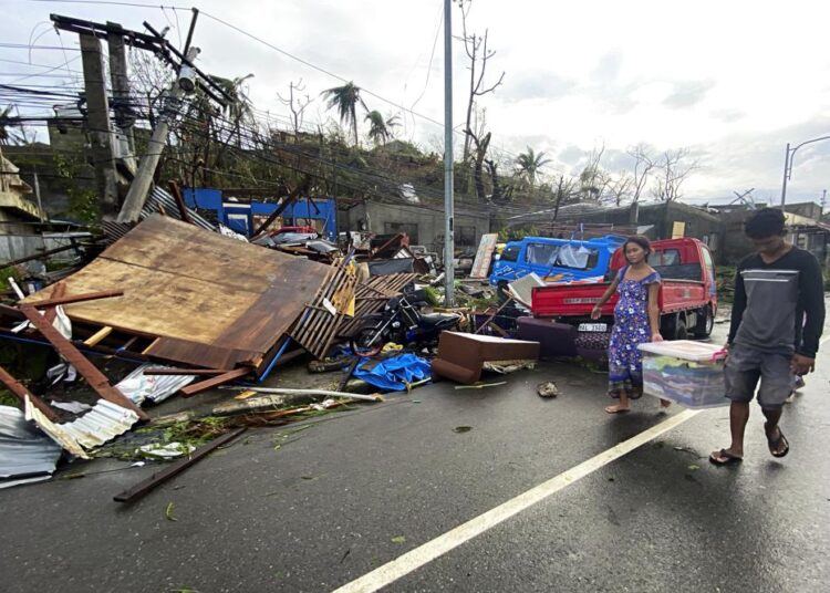 Residents carry what's left of their belongings as they walk past damaged homes due to Typhoon Rai in Surigao city, Surigao del Norte, central Philippines yesterday. A powerful typhoon left more than a dozen people dead, knocked down power and communications in entire provinces and wrought widespread destruction mostly in the central Philippines, officials said Saturday.