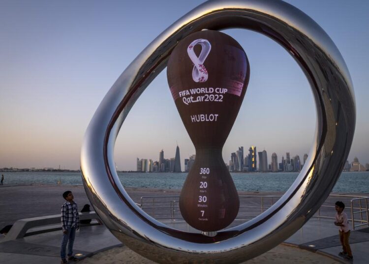 FILE - Children stand next to the official countdown clock showing remaining time until the kick-off of the World Cup 2022, in Doha, Qatar, Nov. 25, 2021. Fans can start registering for the lottery to buy Qatar World Cup tickets Wednesday, Jan. 19, 2022. FIFA tickets will be distributed through a ballot process rather than an open sale for the Nov. 21-Dec. 18 tournament.