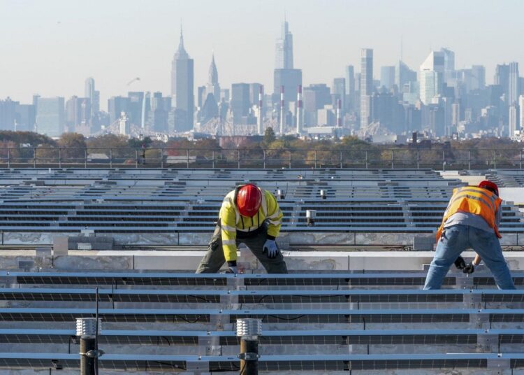 Framed by the Manhattan skyline electricians with IBEW Local 3 install solar panels on top of the Terminal B garage at LaGuardia Airport, on Nov. 9, 2021, in the Queens borough of New York.