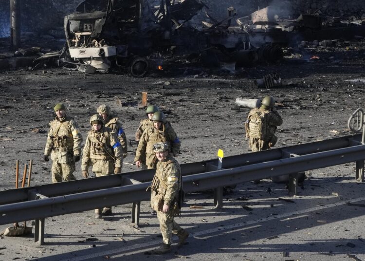 Ukrainian soldiers walk past debris of a burning military truck on a street in Kyiv, Ukraine, Saturday, Feb. 26, 2022.
