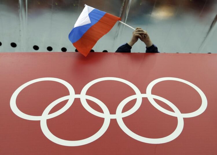 FILE - A Russian flag is held above the Olympic Rings at Adler Arena Skating Center during the Winter Olympics in Sochi, Russia on Feb. 18, 2014.