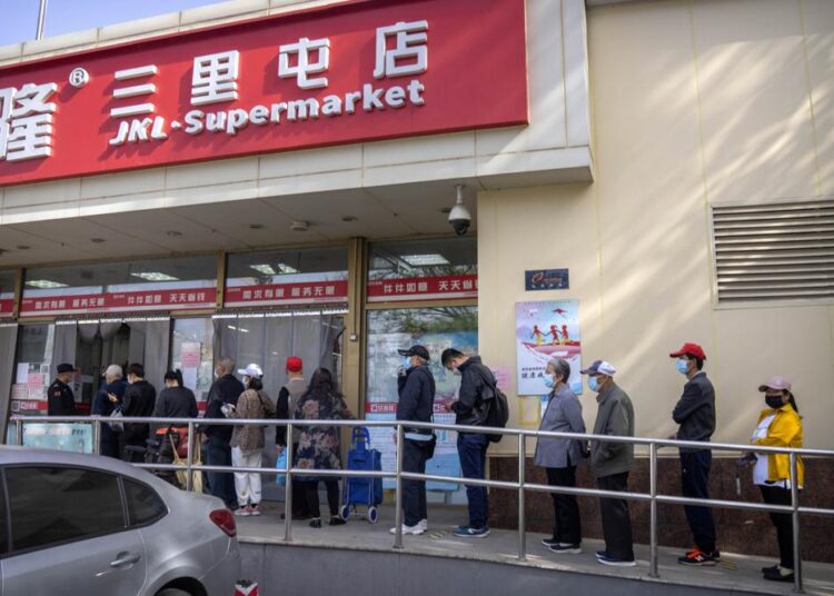 People wearing face masks line up outside a supermarket in Beijing, Tuesday, April 26, 2022.