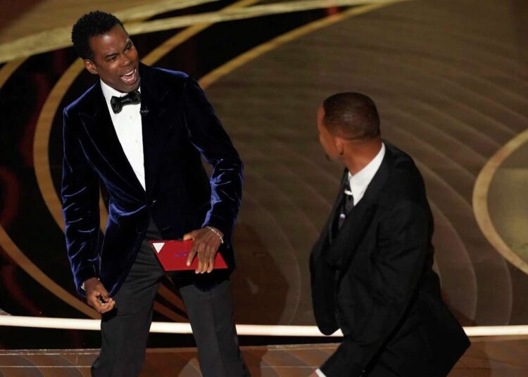 Presenter Chris Rock, left, reacts after being hit on stage by Will Smith while presenting the award for best documentary feature at the Oscars on March 27, 2022, at the Dolby Theatre in Los Angeles.