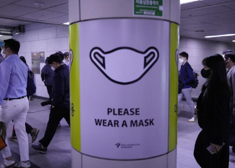 People wearing face masks pass by a poster reminding precautions against the coronavirus at a subway station in Seoul, South Korea, Friday, April 29, 2022.