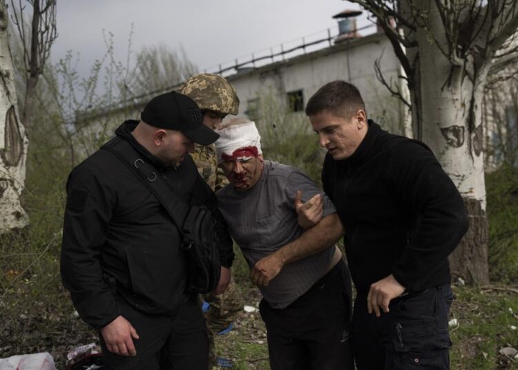 Member of security forces help an injured man following a Russian bombing of a factory in Kramatorsk, eastern Ukraine, on Tuesday, April 19, 2022, killing at least one person and injuring three others.