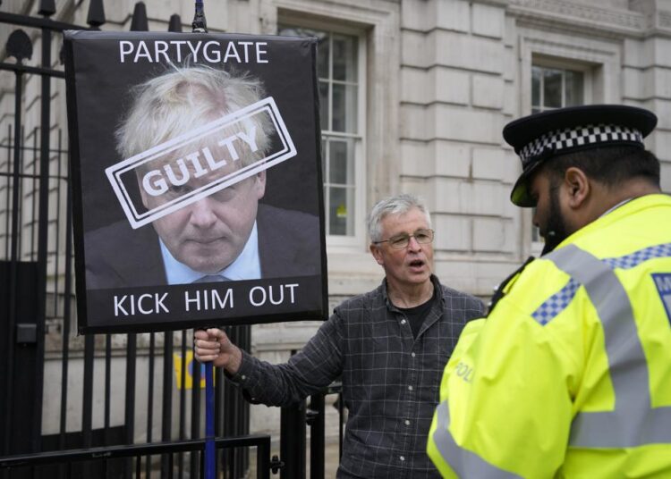A police officer talks to a protester holding up a sign showing British Prime Minister Boris Johnson, in front of the entrance to Downing Street in London, on Wednesday, April 13, 2022.