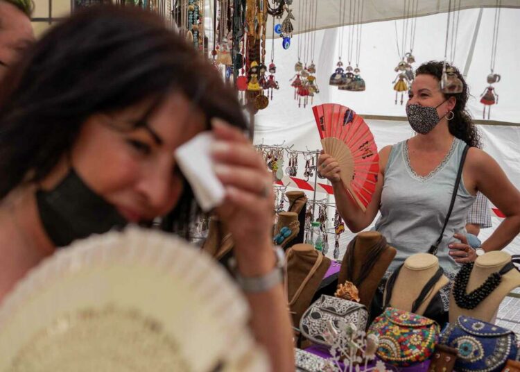 Women cool themselves with fans in the Rastro flea market during a heatwave in Madrid, Spain, Aug. 15, 2021.