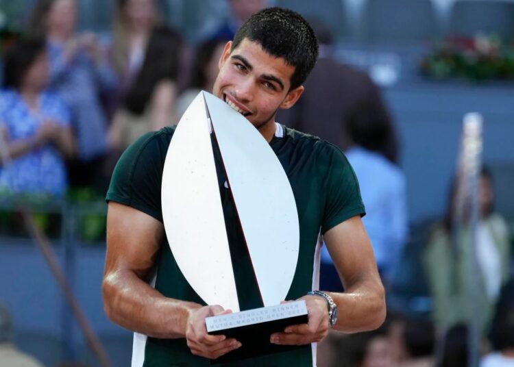 Carlos Alcaraz bites the trophy after winning the final match against Alexander Zverev at the Madrid Open tennis tournament.