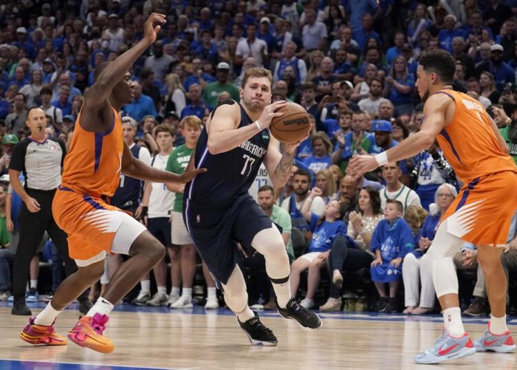 Dallas Mavericks Luka Doncic (C) drives to the basket as Phoenix Suns Bismack Biyombo (L) and Devin Booker defend during their Game 4 of an NBA basketball playoff series in Dallas.