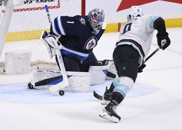 Winnipeg Jets' goaltender Eric Comrie (1) makes a save against Seattle Kraken's Ryan Donato (9) during the second period of NHL hockey game action in Winnipeg, Manitoba.