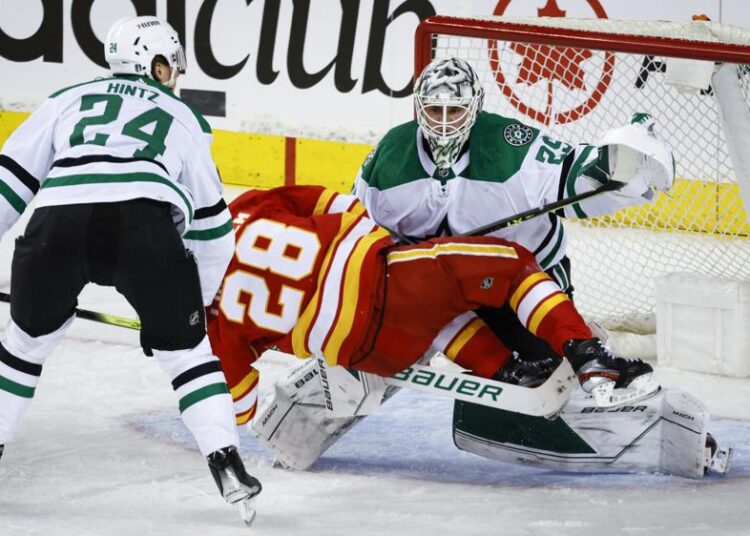 Dallas Stars goalie Jake Oettinger, right, defends as Calgary Flames center Elias Lindholm, front left, tries to score while being checked by Stars center Roope Hintz during the second period of Game 1 of an NHL hockey first-round playoff series in Calgary, Alberta.