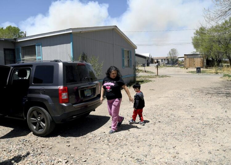Martina Gonzales and her grandson, Lukas Lee Mora, 4, walk outside of their home in Las Vegas, N.M., as a plume of smoke rises in the on Tuesday, May, 3, 2022.