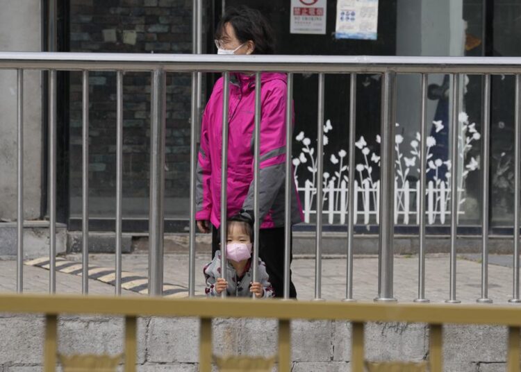 A child wearing a mask looks out from a barrier near closed shops on Monday, May 9, 2022, in Beijing.