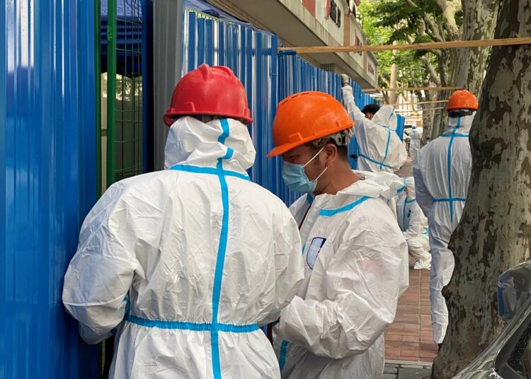 Workers in protective suits set up barriers outside a building, following the coronavirus disease (COVID-19) outbreak, in Shanghai, China June 9, 2022.