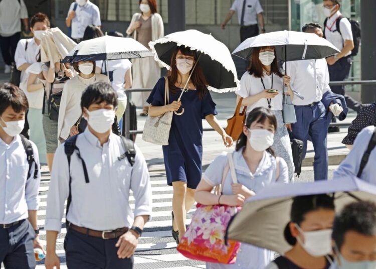 People, some of them holding parasols, cross an intersection amid heat, in Tokyo, Monday, June 27, 2022. Japan’s government issued a warning for possible power crunch in the Tokyo area Monday, asking offices and residents to save energy as the capital region is hit by sweltering heat, with weather officials announcing an earliest end to the rainy season in decades.