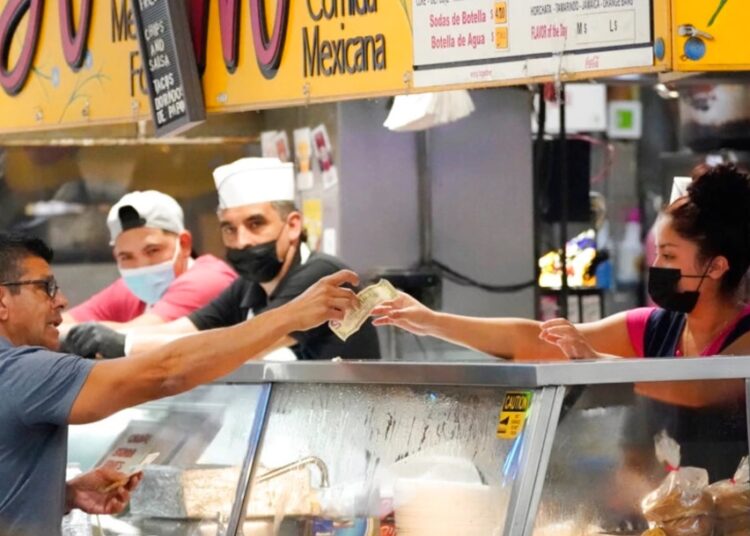 Money is exchanged at a food stand while workers wear face masks inside Grand Central Market on July 13, 2022, in Los Angeles.