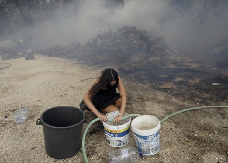 A young woman fills buckets with water for local residents trying to stop a forest fire from reaching their homes in the village of Figueiras, outside Leiria, central Portugal, Tuesday, July 12, 2022.