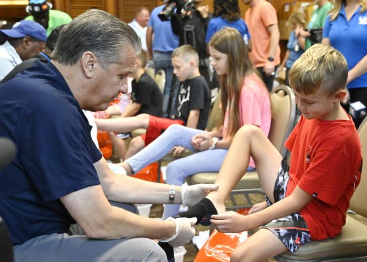 University of Kentucky men's head basketball coach John Calipari, (L), putting socks on one of the kids whose families have been displaced from the eastern Kentucky flooding at a shoe giveaway for flood victims at Jenny Wiley State Park in Prestonsburg, Ky., on Tuesday, August 23, 2022.