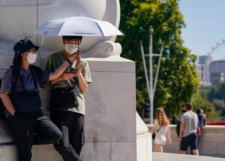 Tourists shelter from the sun under an umbrella as they stand on Queen Victoria Memorial, in London, Aug. 11, 2022.