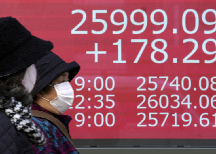 People walk in front of an electronic stock board showing Japan's Nikkei 225 index at a securities firm Friday, Jan. 6, 2023, in Tokyo.
